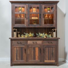 a wooden hutch with glass doors and pine branches on the top, in front of a white wall