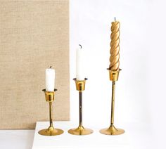 two candles are sitting next to each other on a white surface with a beige wall behind them