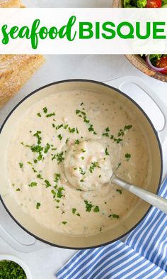 an image of a bowl of seafood bisque with bread and salad in the background