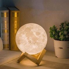 the moon lamp is sitting on top of a table next to books and a potted plant