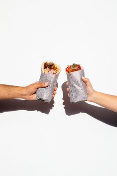 two people holding food in their hands against a white background