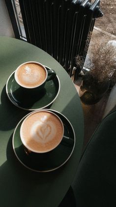 two cups of cappuccino sit on a green table