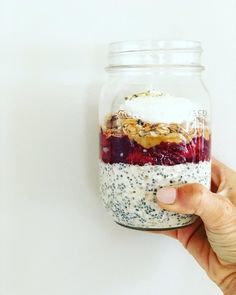 a hand holding a jar filled with fruit and oatmeal desserts on top of each other