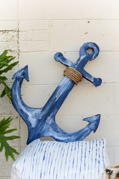 a blue anchor sitting on top of a pillow next to a brick wall and potted plant