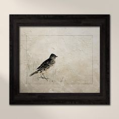 a bird sitting on top of a white wall next to a black framed artwork piece