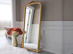 a large gold framed mirror sitting on top of a white rug next to a vase with flowers