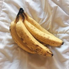 three ripe bananas sitting on top of a white bed sheet covered in black speckles