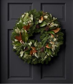 a wreath is hanging on the door with pine cones and greenery around it's edges