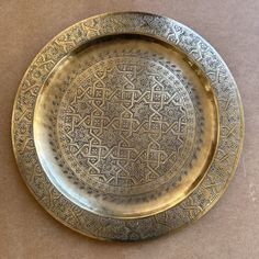 a decorative metal plate with intricate designs on it's rim, sitting on a brown surface