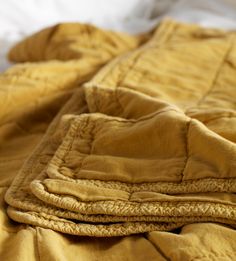 an unmade bed with yellow sheets and pillows