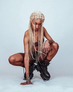 a woman with long blonde hair and boots kneeling on the ground in front of a gray background