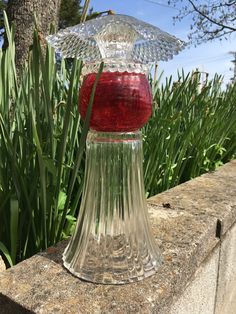 a clear glass candle holder sitting on top of a stone wall next to grass and trees