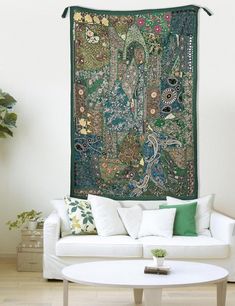 a living room with a large tapestry hanging on the wall above a white couch and coffee table