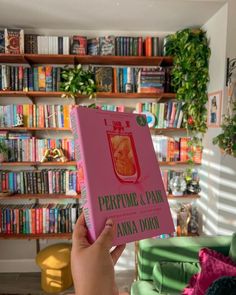 a person holding up a pink book in front of a bookshelf