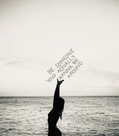 a woman standing on top of a beach next to the ocean holding up a handwritten message