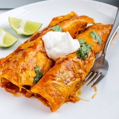 a white plate topped with enchiladas covered in sour cream and garnished with cilantro