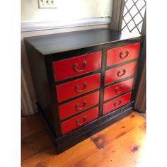 a red and black dresser sitting on top of a wooden floor next to a window