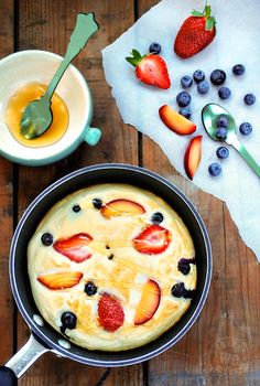 a pancake with blueberries and strawberries in it next to a bowl of fruit