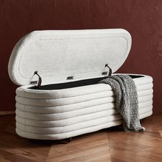 an upholstered storage bench with the lid open on a wooden floor in front of a red wall