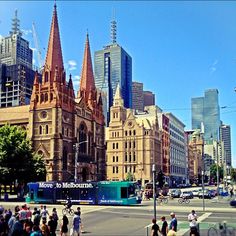 people are walking across the street in front of tall buildings with spires on them