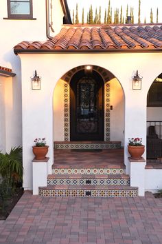 the front entrance to a home with potted plants on the steps and tiled walkway