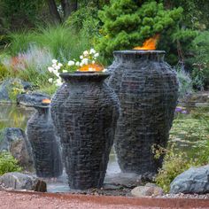 three black vases sitting next to each other in front of a pond and trees