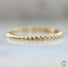 a yellow gold wedding band with twisted rope design on the side, sitting on a white surface