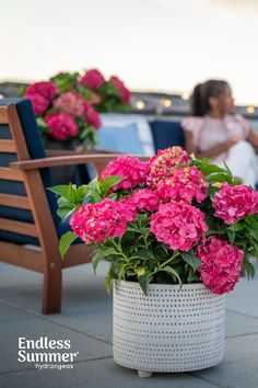 pink flowers are in a white vase on a patio with two women sitting at the end