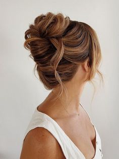 a woman with her hair in a low bun, wearing a white top and looking off to the side