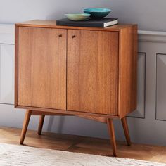 a wooden cabinet with a bowl on top of it next to a rug and wall