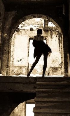 a ballerina is standing on the edge of an old building in black and white