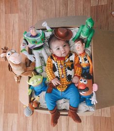 a baby sitting in a cardboard box surrounded by toy characters