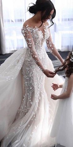 two women in wedding gowns standing next to each other and one is holding the bride's hand