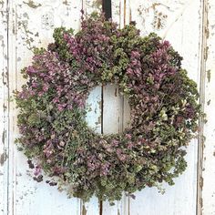 a wreath hanging on the side of a white door with purple flowers and green leaves