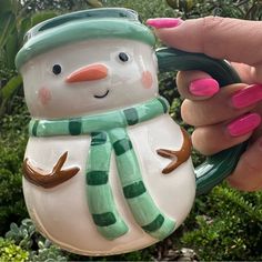 a hand holding a snowman ornament with green and white stripes on it