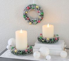 two white candles sitting on top of books next to a wreath and christmas decorations hanging from the wall