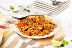 a white plate topped with pasta and meat next to lime wedges on a wooden cutting board