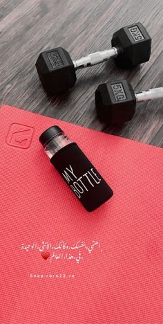 two dumbbells and a bottle of water on top of a red yoga mat