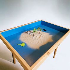 a small table with sand and plants on the top, in front of a white background