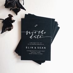 black wedding save the date cards with calligraphy on them next to dried rose petals