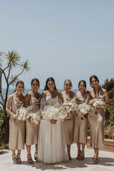 a group of women standing next to each other in front of the ocean holding bouquets