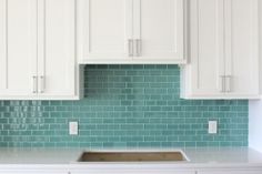 a kitchen with white cabinets and green tile backsplash