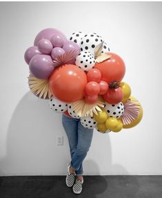 a woman standing in front of a wall holding balloons