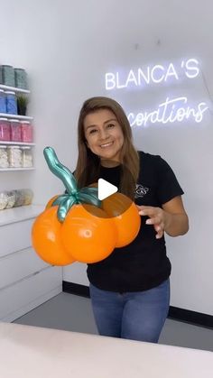 a woman holding an orange balloon in front of a white wall with the words blanca's creations on it