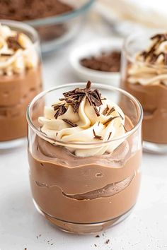 three desserts in small glass dishes on a white countertop with chocolate and whipped cream