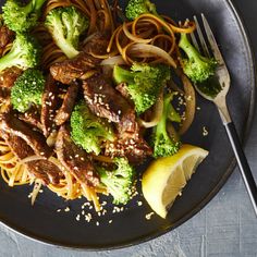 a black plate topped with meat and broccoli covered in sesame seeds next to a fork