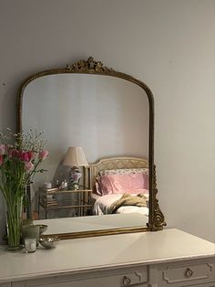 a mirror sitting on top of a dresser next to a vase with flowers in it