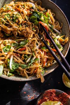 a bowl filled with noodles, meat and veggies next to chopsticks