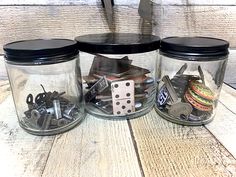 three glass jars filled with different types of buttons and screws on top of a wooden table