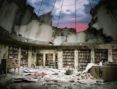 an abandoned library with bookshelves and broken glass in the ceiling is shown under a cloudy sky